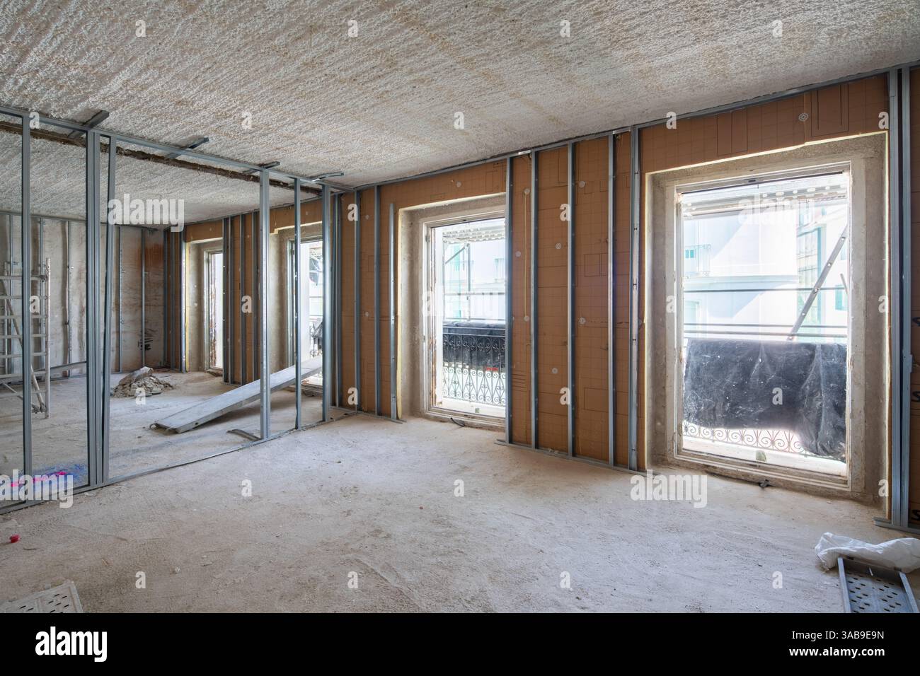 Une pièce lumineuse et vide en cours de rénovation, présentant des cadres muraux métalliques apparents et de grandes ouvertures de fenêtres. L'espace est éclairé par la lumière naturelle, réfléchissante Banque D'Images