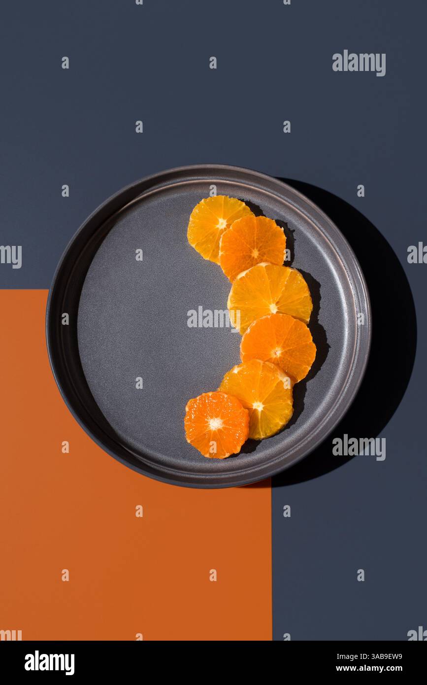 Arrangement artistique de tranches d'orange et de mandarine sur une assiette sombre, sur un fond saisissant d'orange et de noir. Met en valeur des couleurs éclatantes A. Banque D'Images