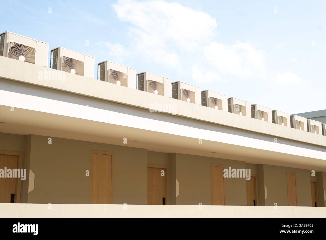 Une rangée d'unités de climatisation sur un toit de bâtiment moderne contre un ciel bleu clair en Thaïlande. L'extérieur beige avec portes en bois crée un mini Banque D'Images