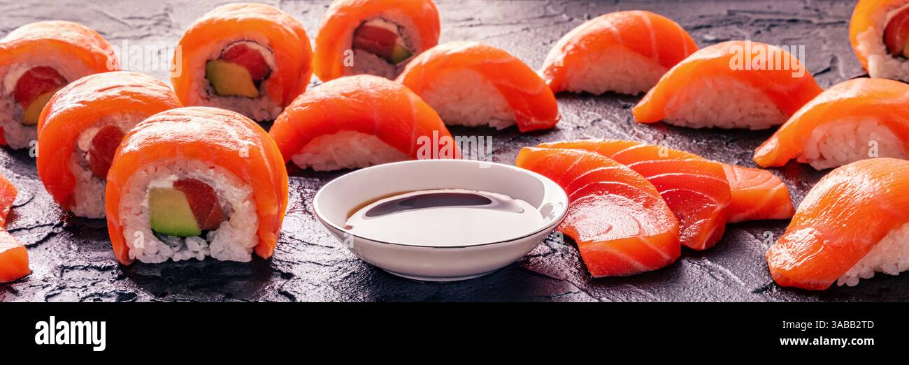 Ensemble de rouleaux de sushi uramaki au saumon, tranches de sashimi, nigiri et sauce soja, panorama sur fond d'ardoise noire, bannière panoramique Banque D'Images