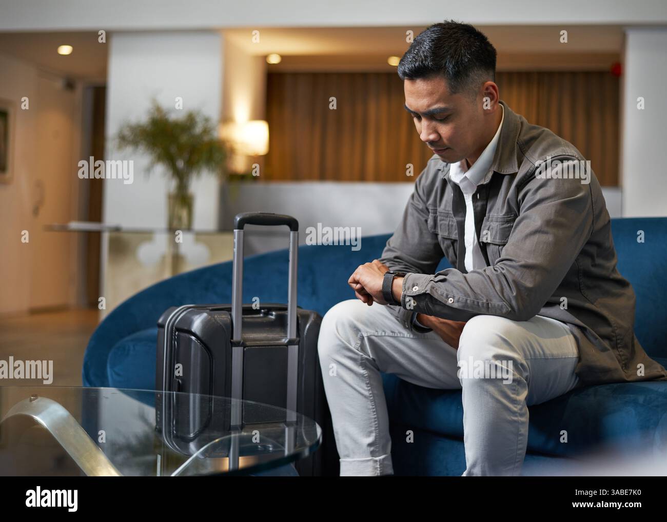 Voyageur attendant dans le hall de l'hôtel avec bagages pendant la vérification de l'heure Banque D'Images