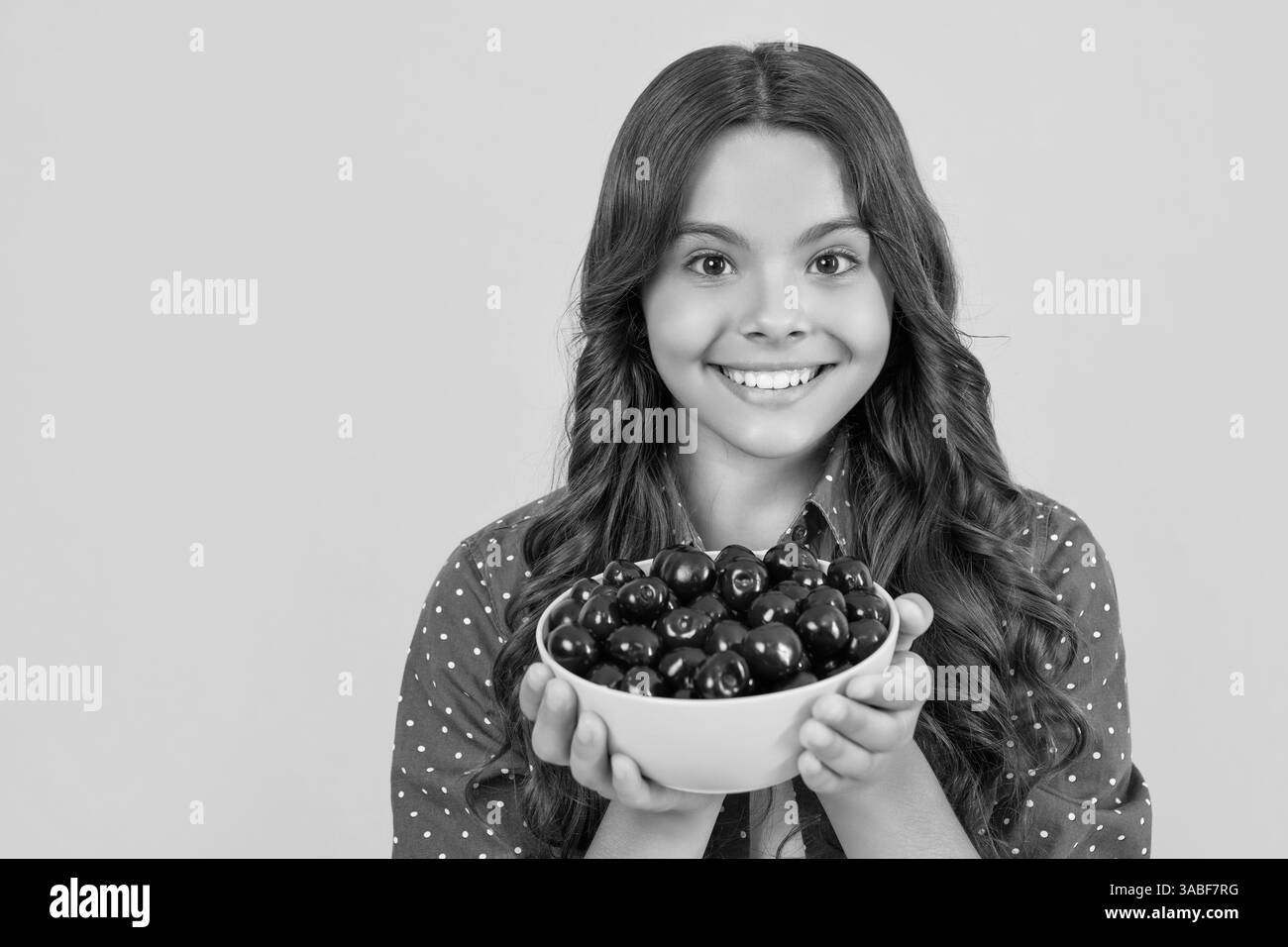bonne fille de l'adolescence tenir le bol de cerise sur fond jaune. copier l'espace Banque D'Images