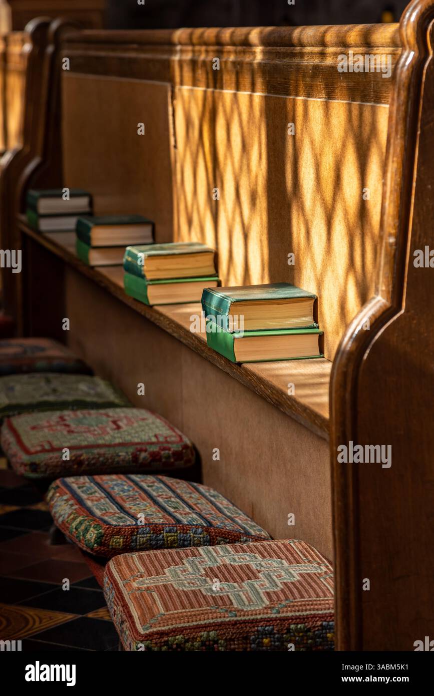 Genouillères de tapisserie et livres d'hymnes prêts dans un banc en bois pour un service à l'église Banque D'Images