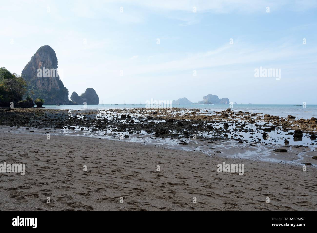 La marée basse sur la plage de Tonsai révèle des textures rocheuses et des falaises calcaires sous un ciel matinal doux Banque D'Images