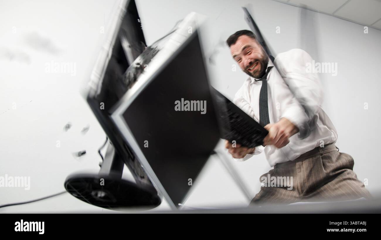 Заголовок : un homme d'affaires agressif perd son sang-froid dans un accès de rage. Un employé de bureau en colère brise un écran d'ordinateur avec son clavier. Banque D'Images