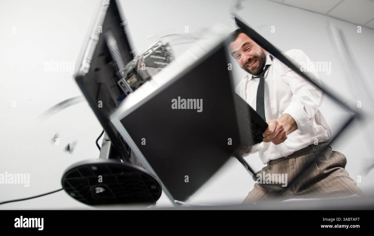 Заголовок : un homme d'affaires agressif perd son sang-froid dans un accès de rage. Un employé de bureau en colère brise un écran d'ordinateur avec son clavier. Banque D'Images