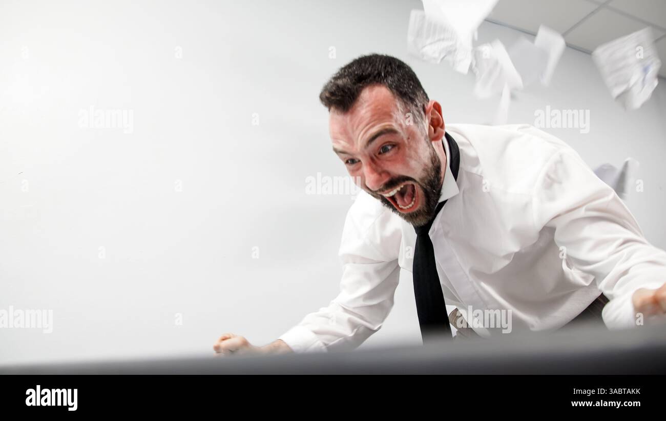 Заголовок : un homme d'affaires agressif perd son sang-froid dans un accès de rage. Un employé de bureau en colère brise un écran d'ordinateur avec son clavier. Banque D'Images