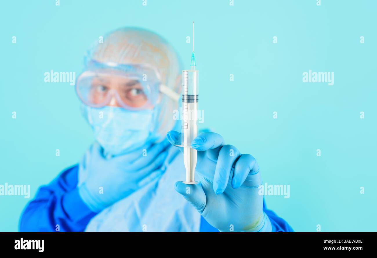 Docteur en uniforme, masque médical et capuchon chirurgical avec seringue. Mise au point sélective. Infirmier ou médecin en combinaison de protection, lunettes et gants en caoutchouc Banque D'Images