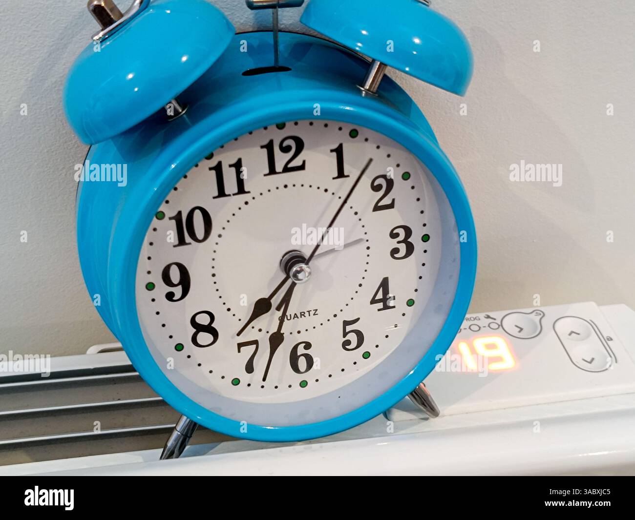 Réveil bleu posé sur un radiateur affichant 19 degrés. Banque D'Images