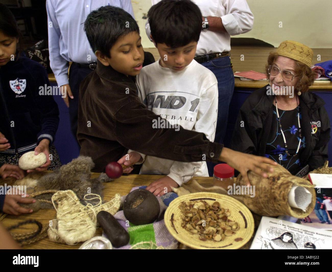 (Publié 04/01/2004, B-1 :1,2 ; UTS1798487) Carlos Lazo, 9 ans, à gauche, atteint Juan Ruiz, 9, au centre, pour une gourde alors que Jane Dumas, aînée de la tribu, membre du village indien Jamul, est assis à proximité. Les élèves de troisième et quatrième année de la Darnall Charter School apprenaient la culture de la tribu Kumeyaay.--Laura Embry/Union-Tribune Banque D'Images
