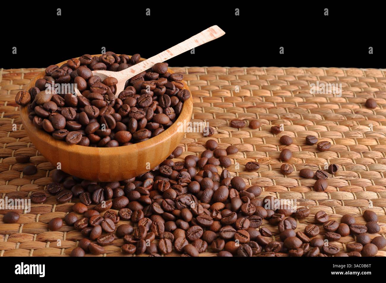 Grains de café bruns se renversant d'un bol en bois avec une cuillère, reposant sur un tapis tissé sous un éclairage doux et chaud, mettant en évidence les textures naturelles Banque D'Images