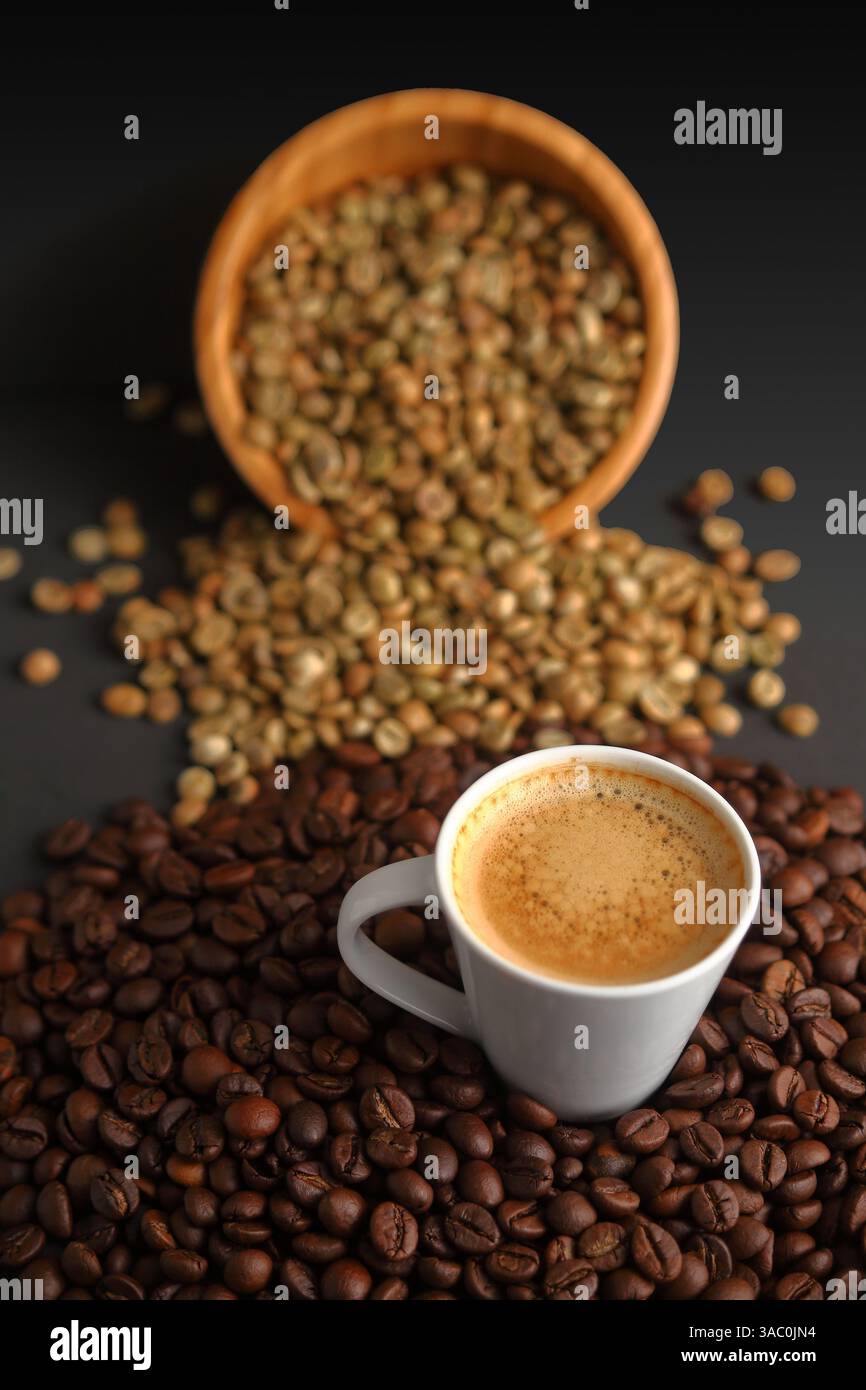 Une tasse de café à la vapeur entourée de grains verts et torréfiés, représentant le voyage du café cru au café infusé Banque D'Images