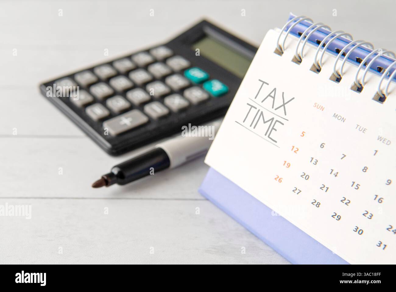 Un calendrier avec « TAX TIME » écrit sur la page supérieure à côté d'une calculatrice et d'un stylo. Concept commercial et financier. Banque D'Images