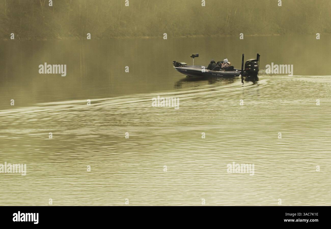 Deux hommes assis dans un bateau de basse sur un lac avec le brouillard du matin pour la pêche de basse Banque D'Images