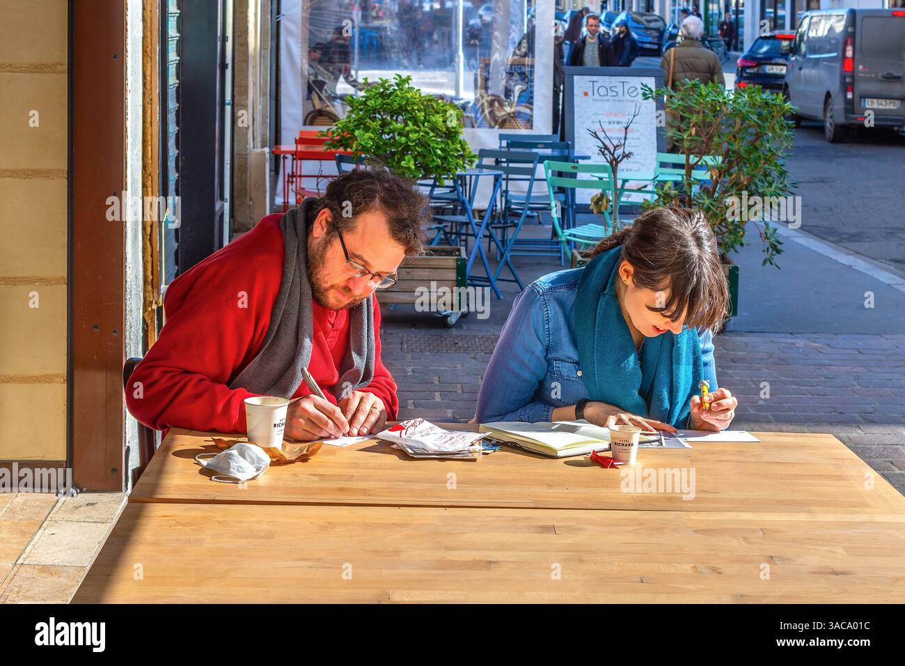 Couple à la table de café extérieur occupé à écrire des cartes postales - Tours, Indre-et-Loire (37), France. Banque D'Images