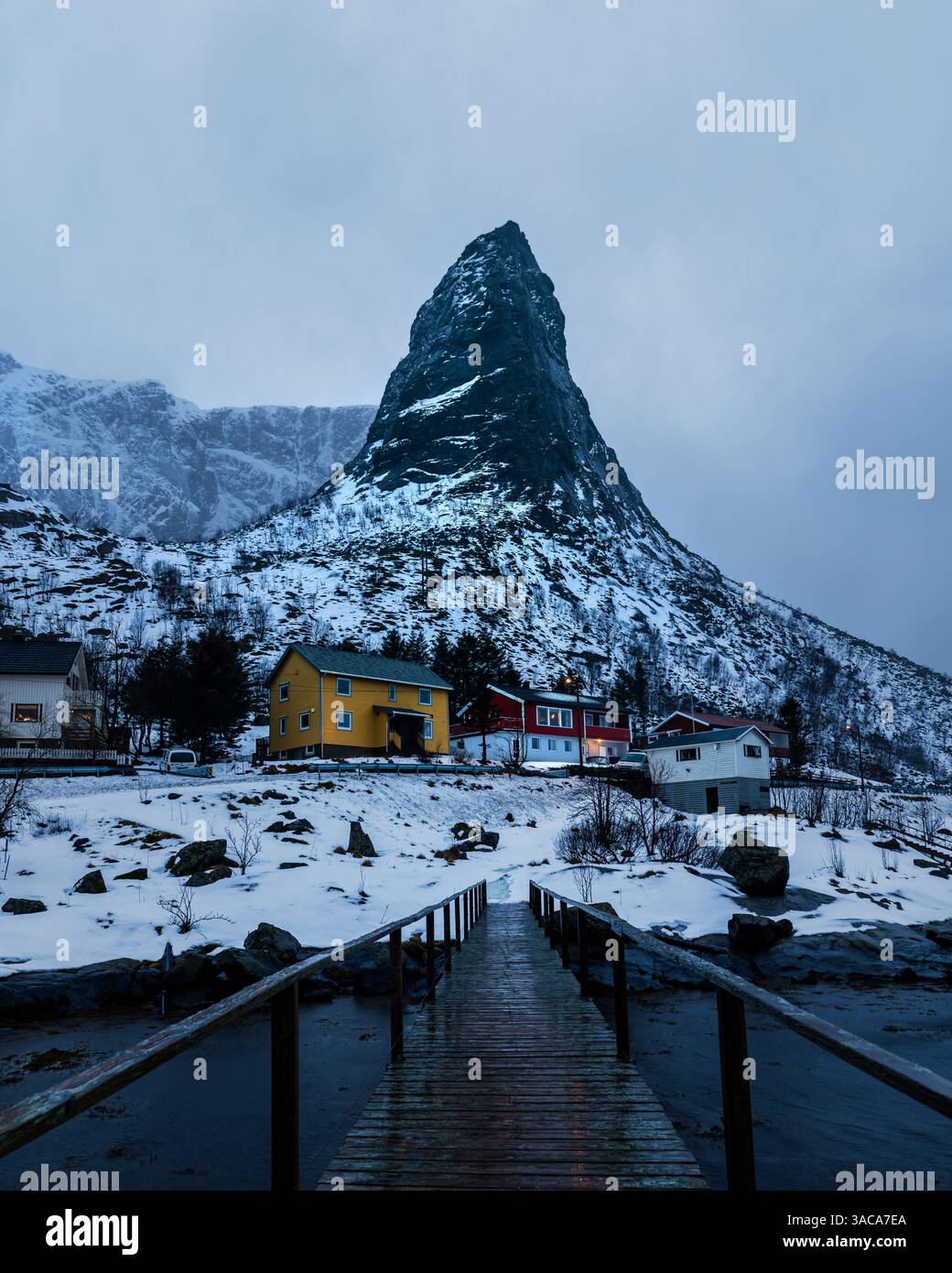 Hammerskråga BEI Reine auf den Lofoten im Winter zur blauen Stunde, verschneite Landschaft mit schmaler Brücke im Vordergrund tiefer stürmischer Wolke Banque D'Images