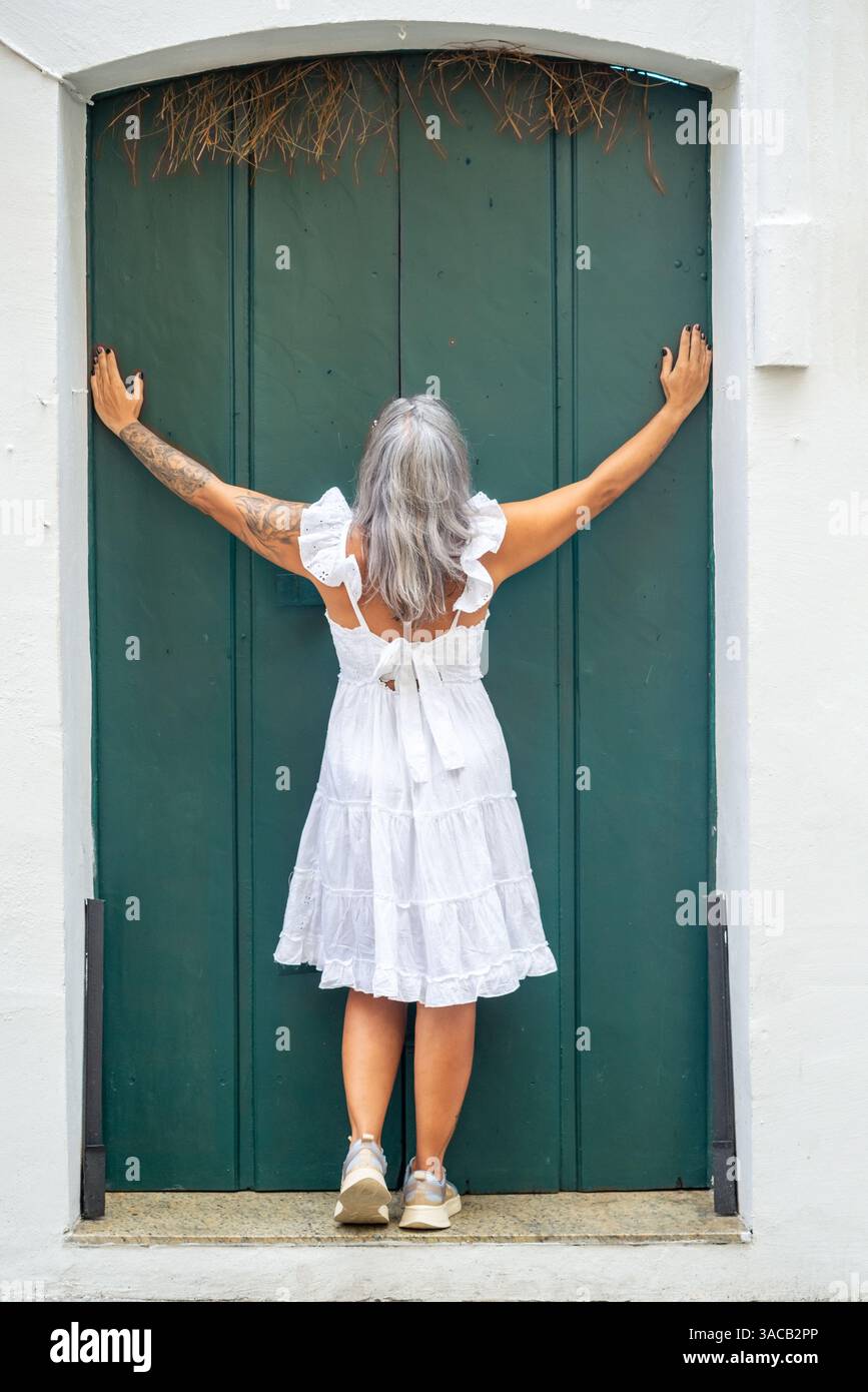 Femme portant une robe blanche appuyée contre une vieille porte de maison. Personne voyageant. Amérique du Sud. Banque D'Images