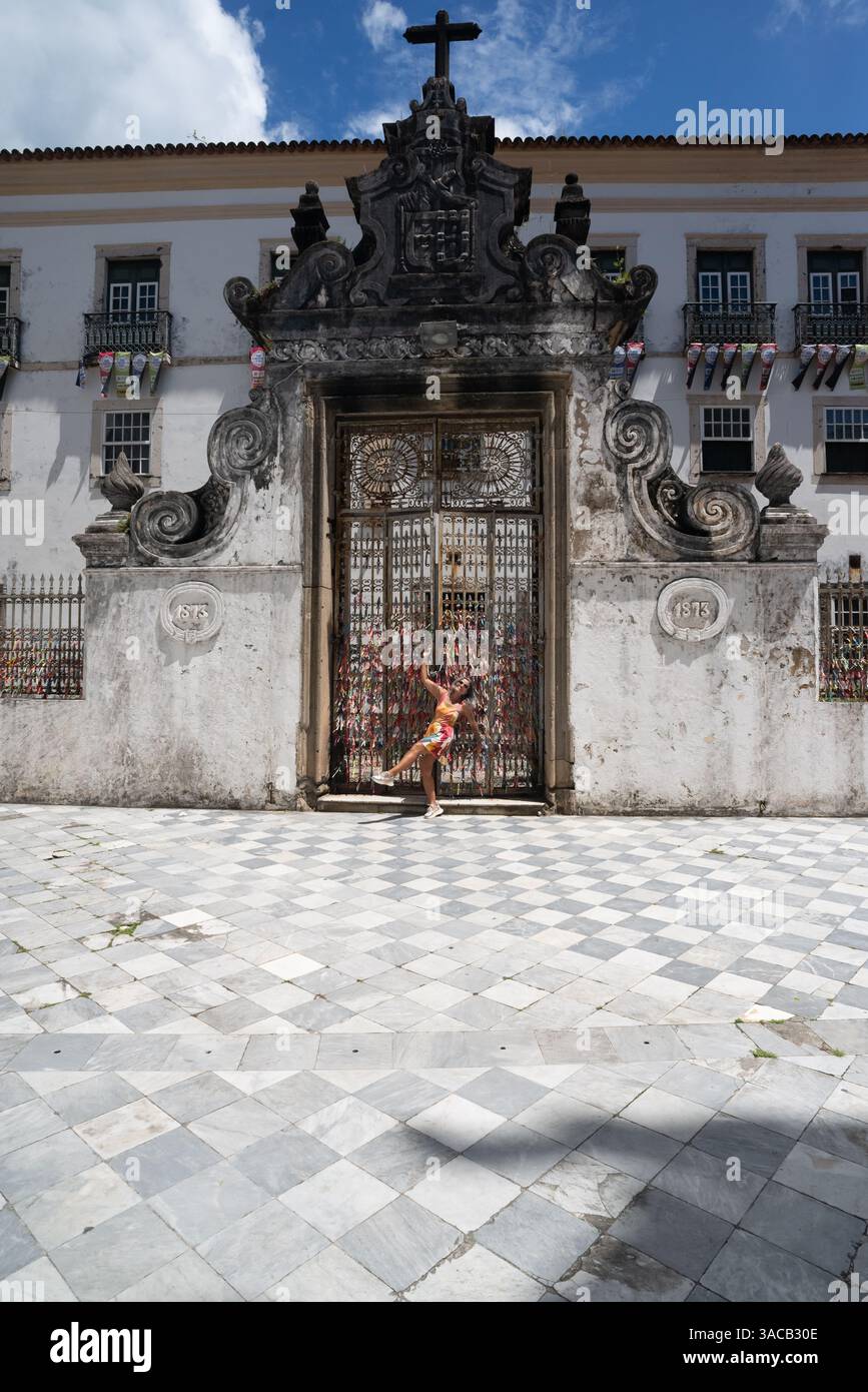 Belle femme vêtue d'une robe blanche et de lunettes de soleil, souriante et heureuse, voyageant, appuyée contre une grande porte d'une église. Amérique du Sud. Banque D'Images