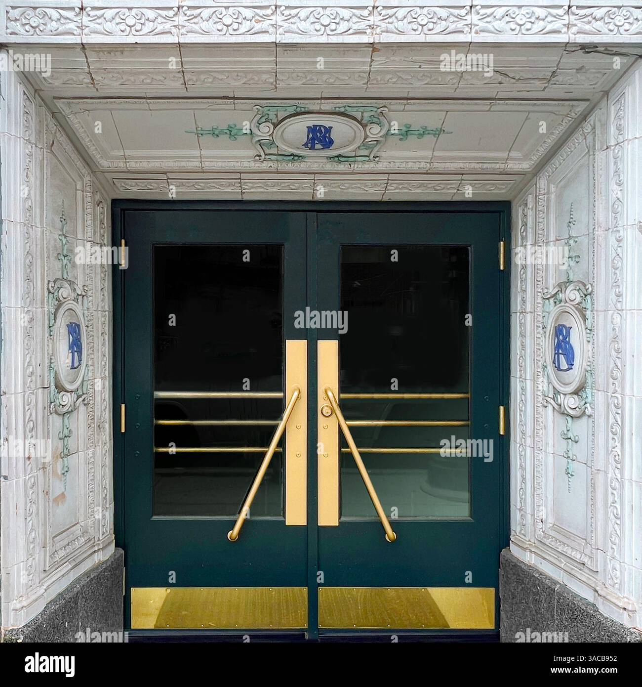 Portes élégantes avec poignées dorées et panneaux vert sarcelle, encadrées par des colonnes en terre cuite blanche ornée de monogrammes bleus dans un Chicago historique. Banque D'Images