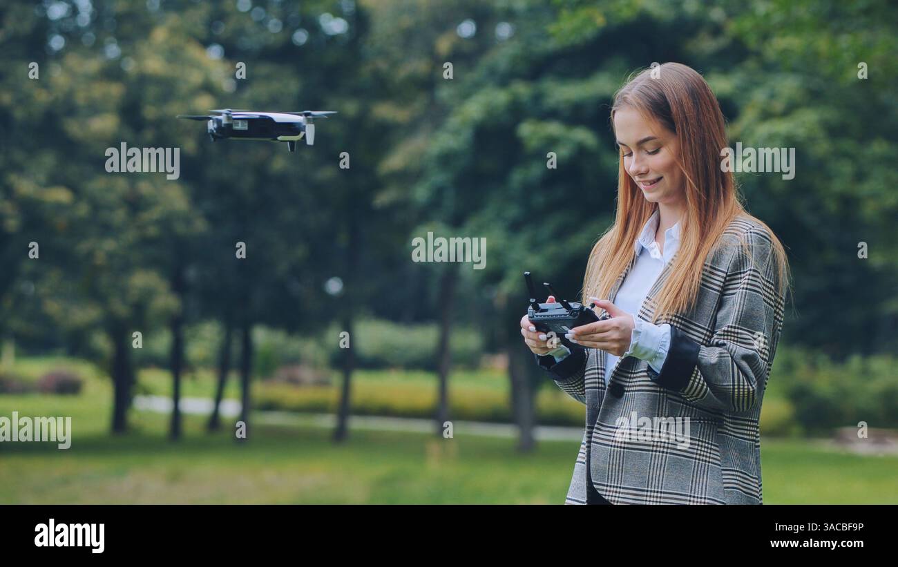 Femme d'affaires exploitant un drone avec télécommande dans le parc vert, profitant de la technologie innovante et de l'exploration aérienne Banque D'Images