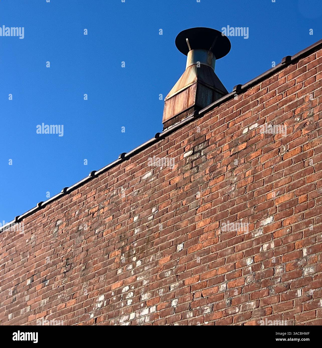 Toit urbain avec une cheminée en métal contre un ciel bleu clair dans un paysage urbain en fin d'après-midi Banque D'Images