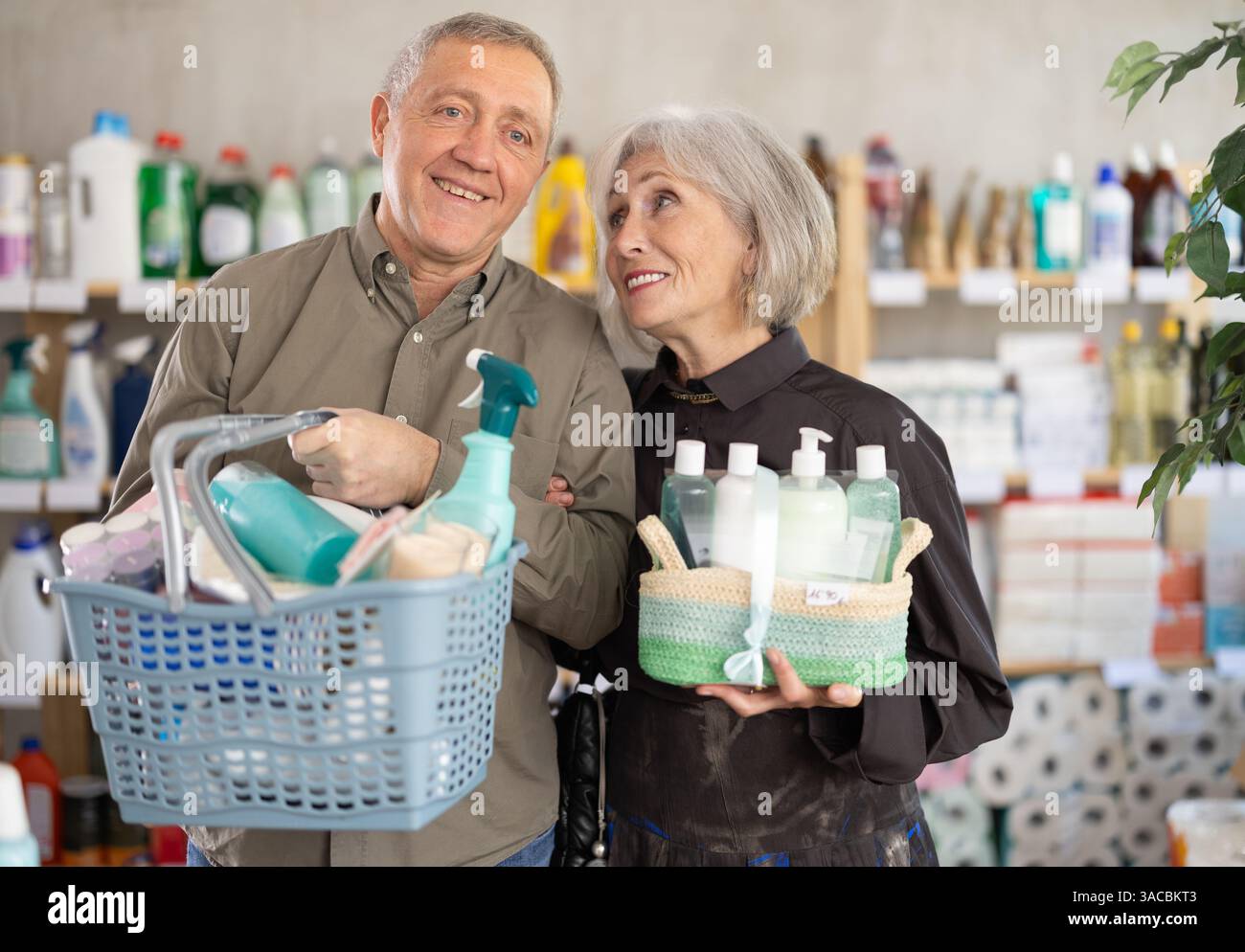 Couple mature avec panier complet choisissant des articles ménagers dans le supermarché Banque D'Images