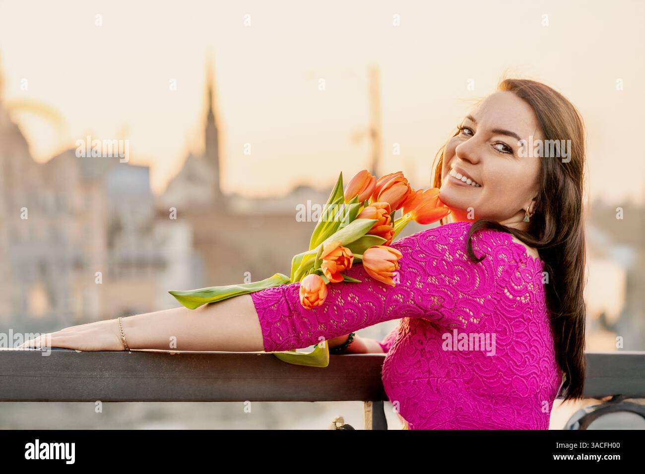 Femme souriant avec des tulipes dans une robe rose au coucher du soleil Banque D'Images