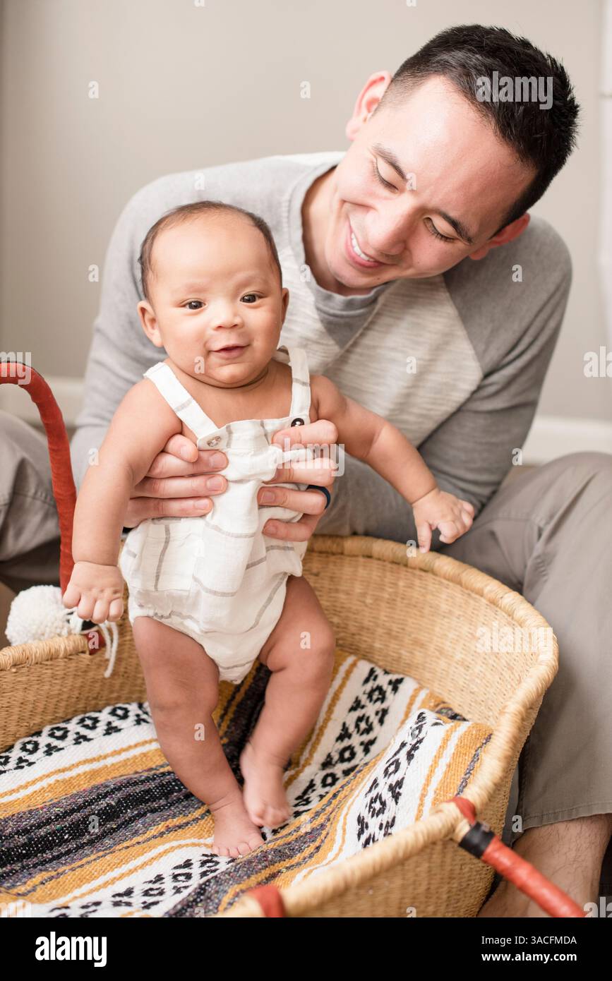 Papa aide bébé à pratiquer debout à l'intérieur d'un panier tissé confortable Banque D'Images