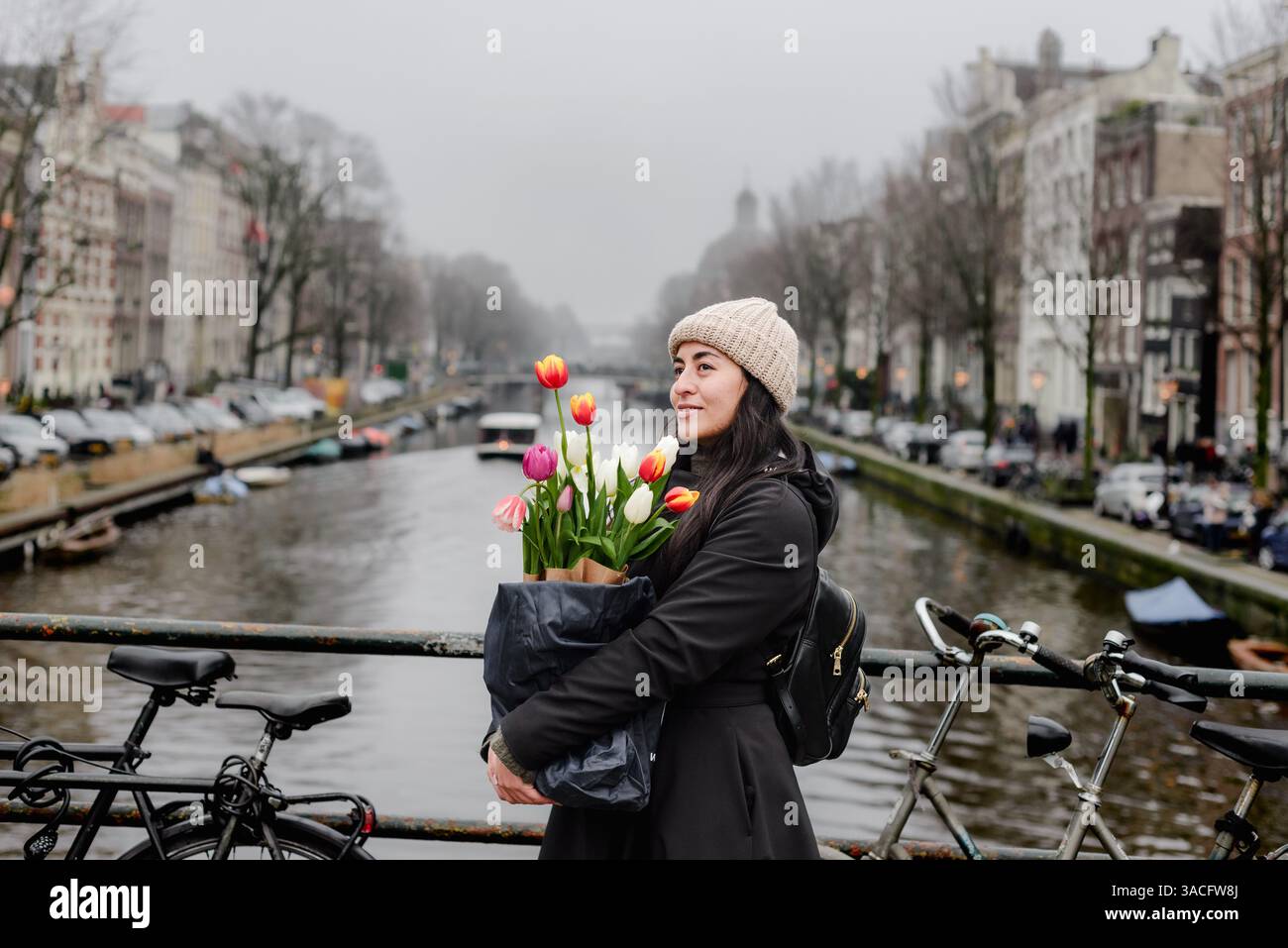Femme tenant des tulipes sur le pont du canal à Amsterdam avec des vélos Banque D'Images