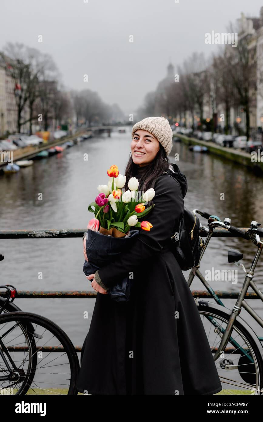 Femme souriante tenant des tulipes en hiver sur Amsterdam canal Bridge Banque D'Images