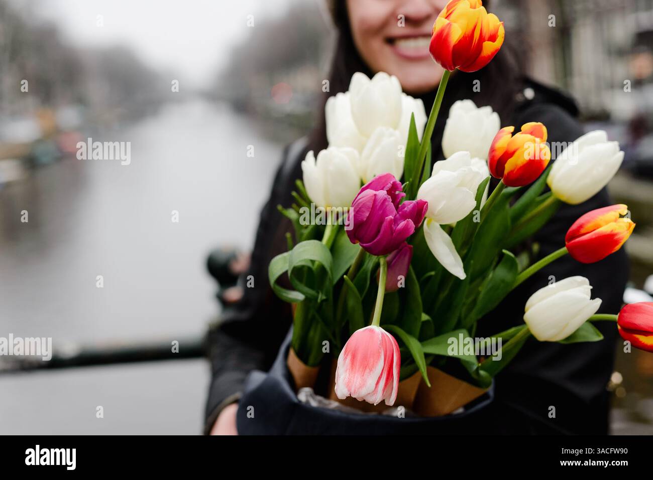 Femme souriante tenant un bouquet de tulipes avec Amsterdam canal en arrière-plan Banque D'Images