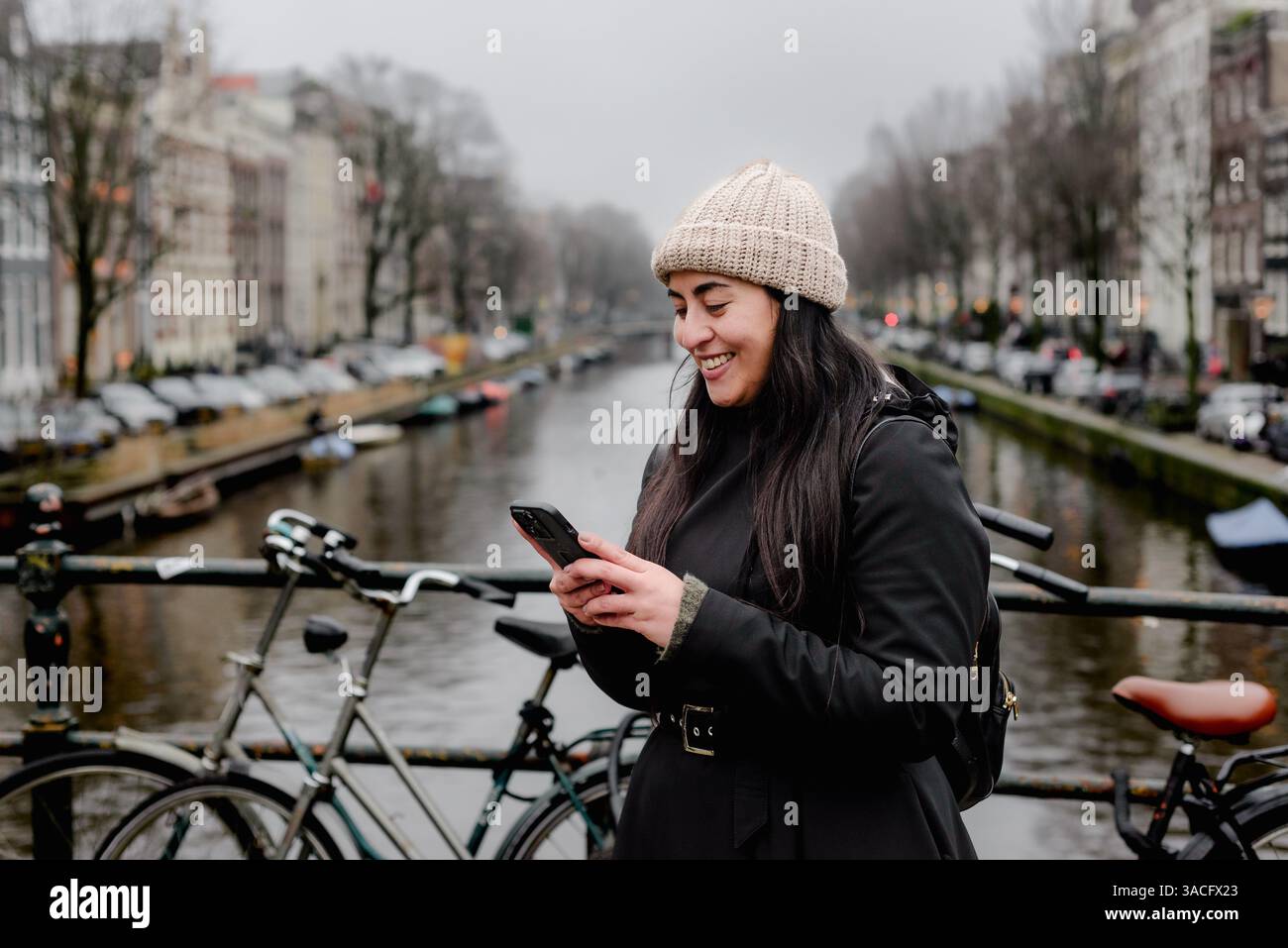 Femme souriant à son téléphone sur le pont d'Amsterdam pendant l'hiver Banque D'Images