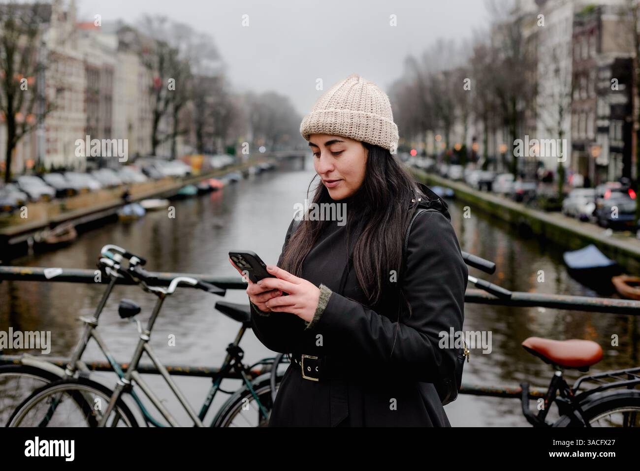 Femme utilisant smartphone sur le pont d'Amsterdam le jour couvert d'hiver Banque D'Images