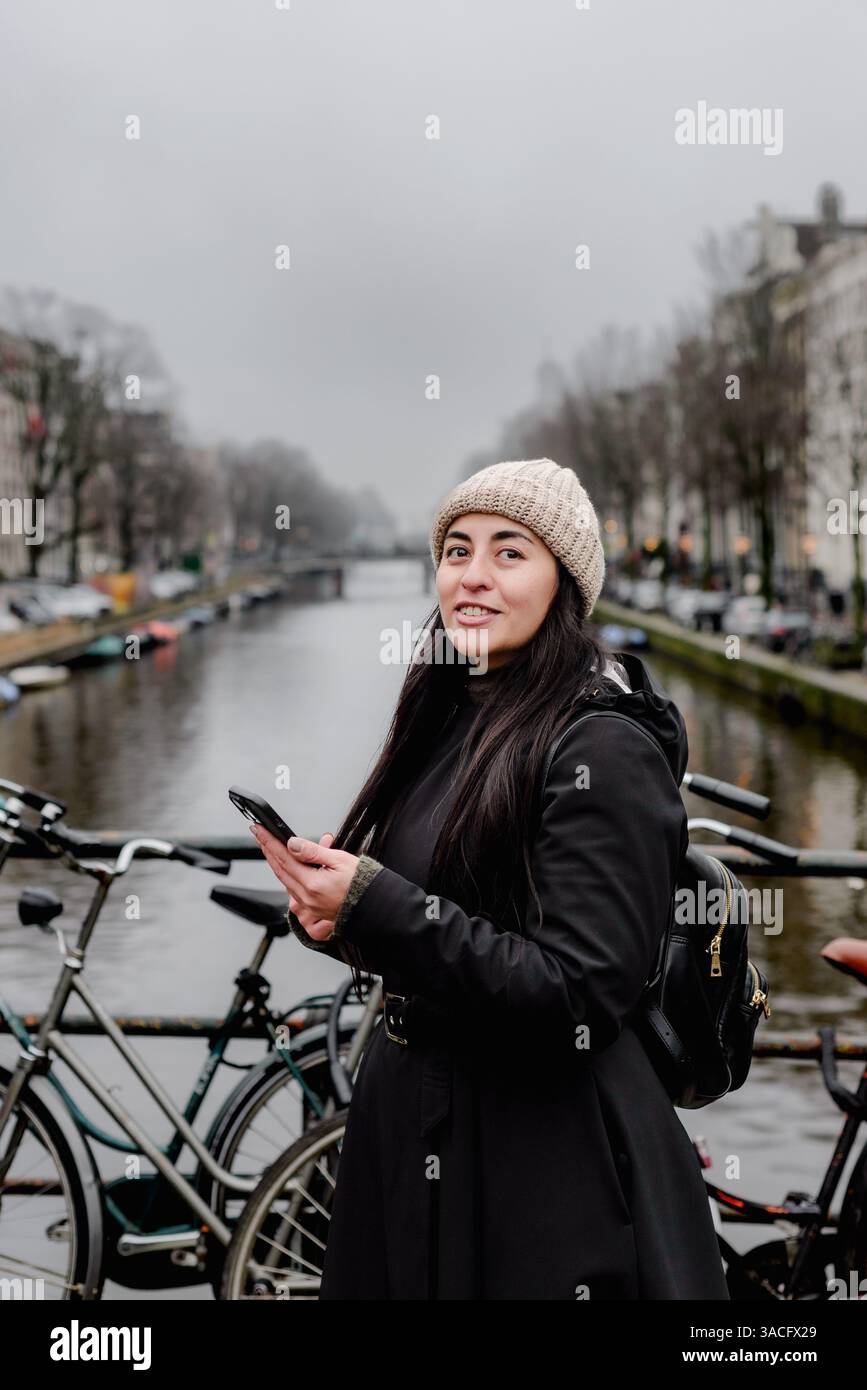 Femme tenant smartphone tout en se tenant debout sur le pont du canal d'Amsterdam Banque D'Images