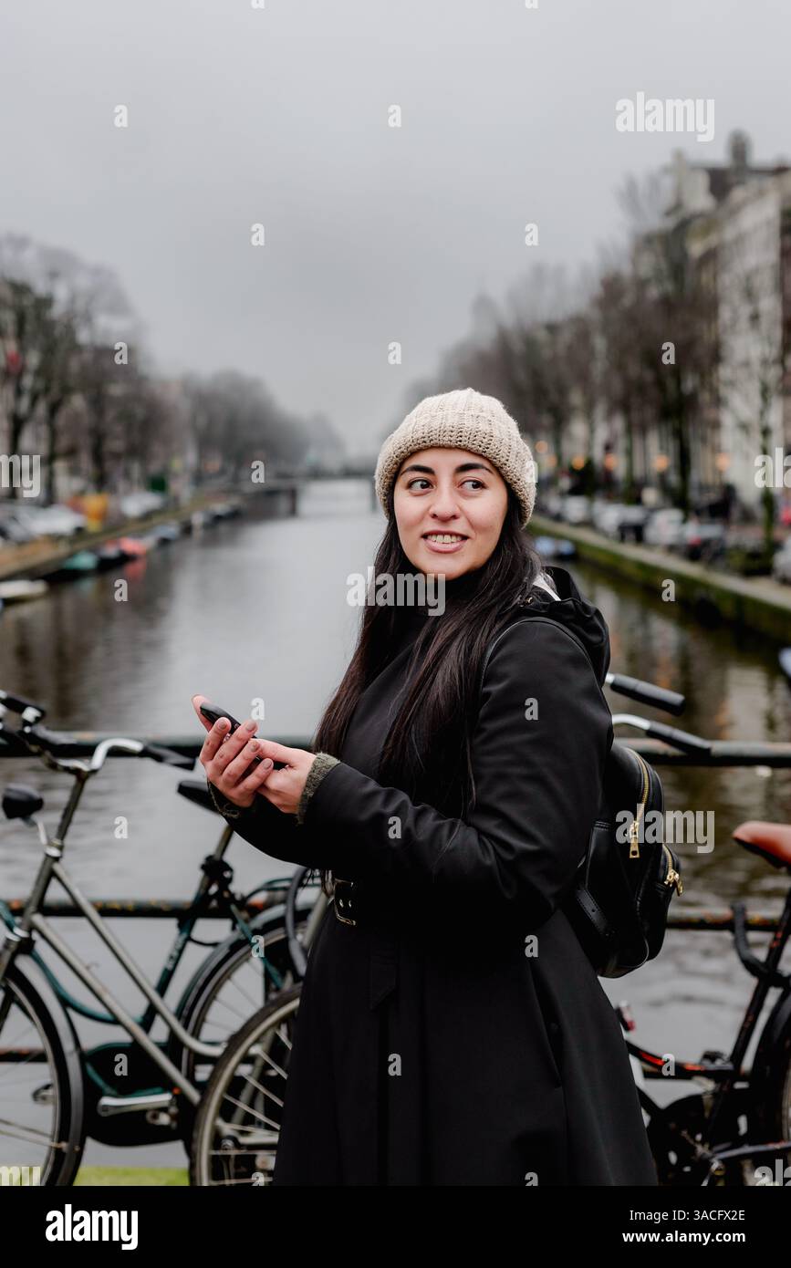 Femme regardant loin tout en tenant téléphone sur Amsterdam canal Bridge Banque D'Images