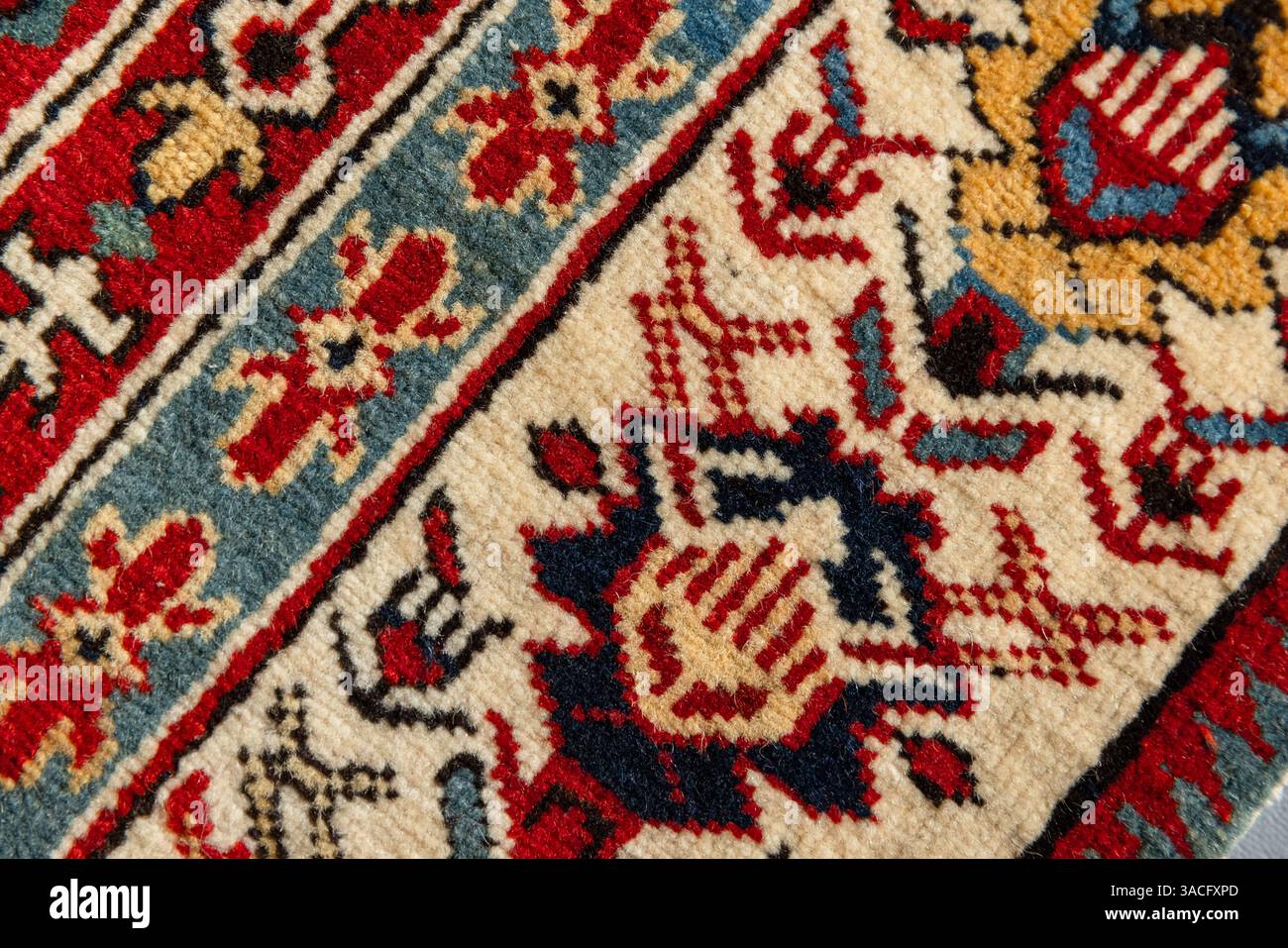 Macro photo d'un vieux tapis oriental en laine fait à la main présentant des motifs floraux et géométriques détaillés dans des tons rouges, bleus, jaunes et crème. Bakou, Azer Banque D'Images
