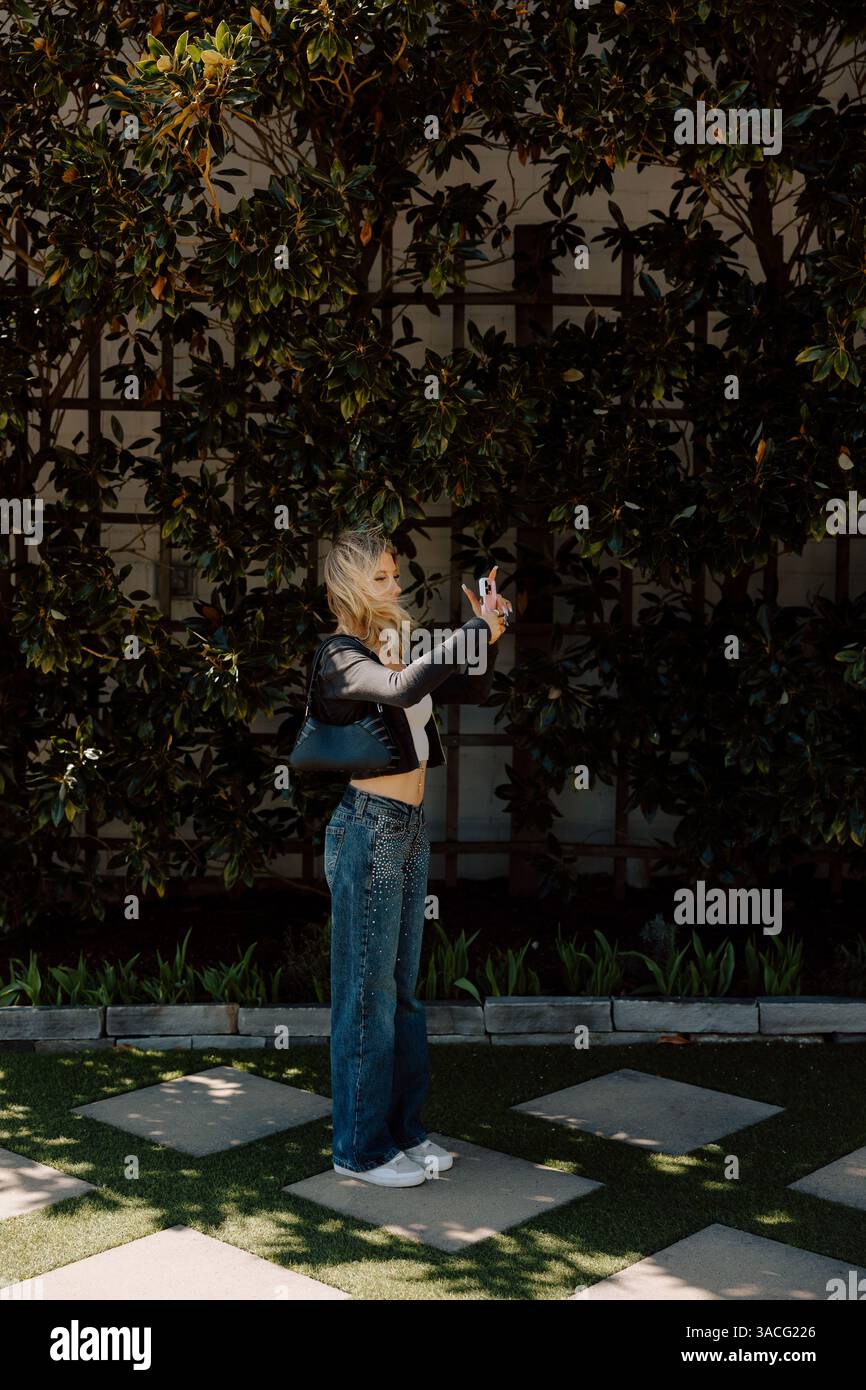 Jeune femme prenant un selfie dans un jardin, vent soufflant Banque D'Images