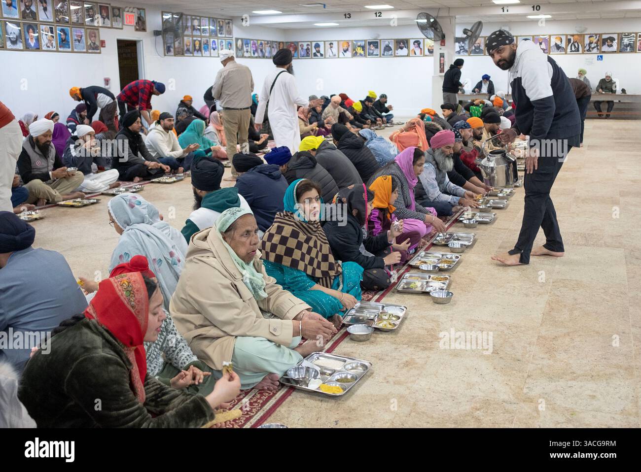 Un serveur bénévole et une foule du dimanche matin dans une cuisine communale langar dans un temple sikh dans le Queens, New York. Banque D'Images
