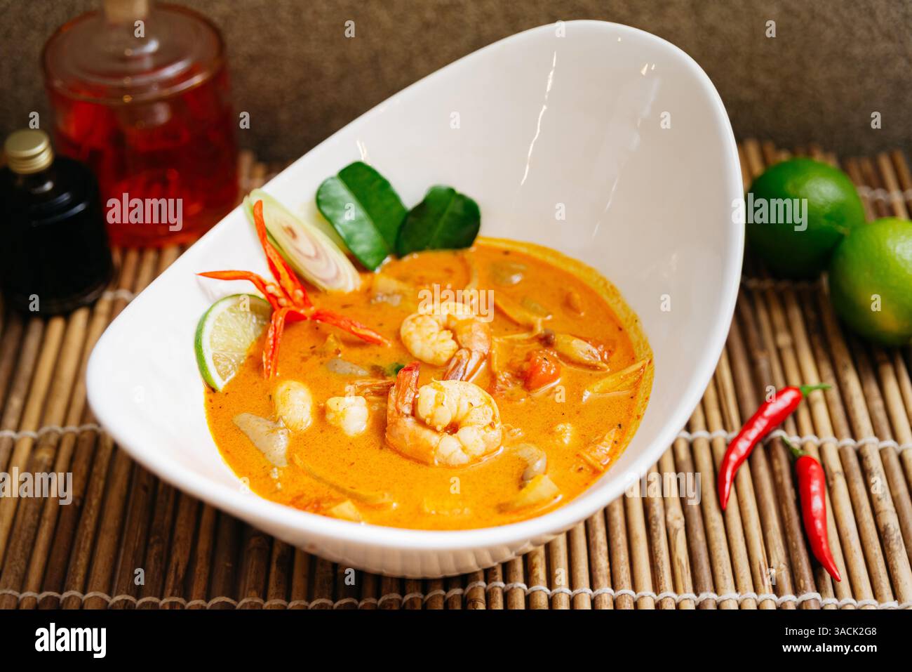 Soupe thaïlandaise tom yum chaude et crémeuse avec crevettes, citronnelle, piment, citron vert et feuilles de kaffir servie dans un bol blanc moderne. Banque D'Images
