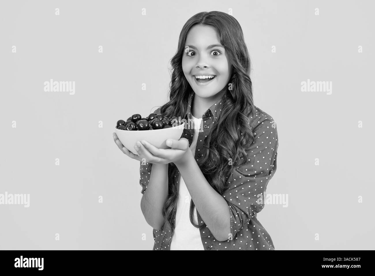 une jeune fille surprise tient un bol de cerise sur fond jaune Banque D'Images