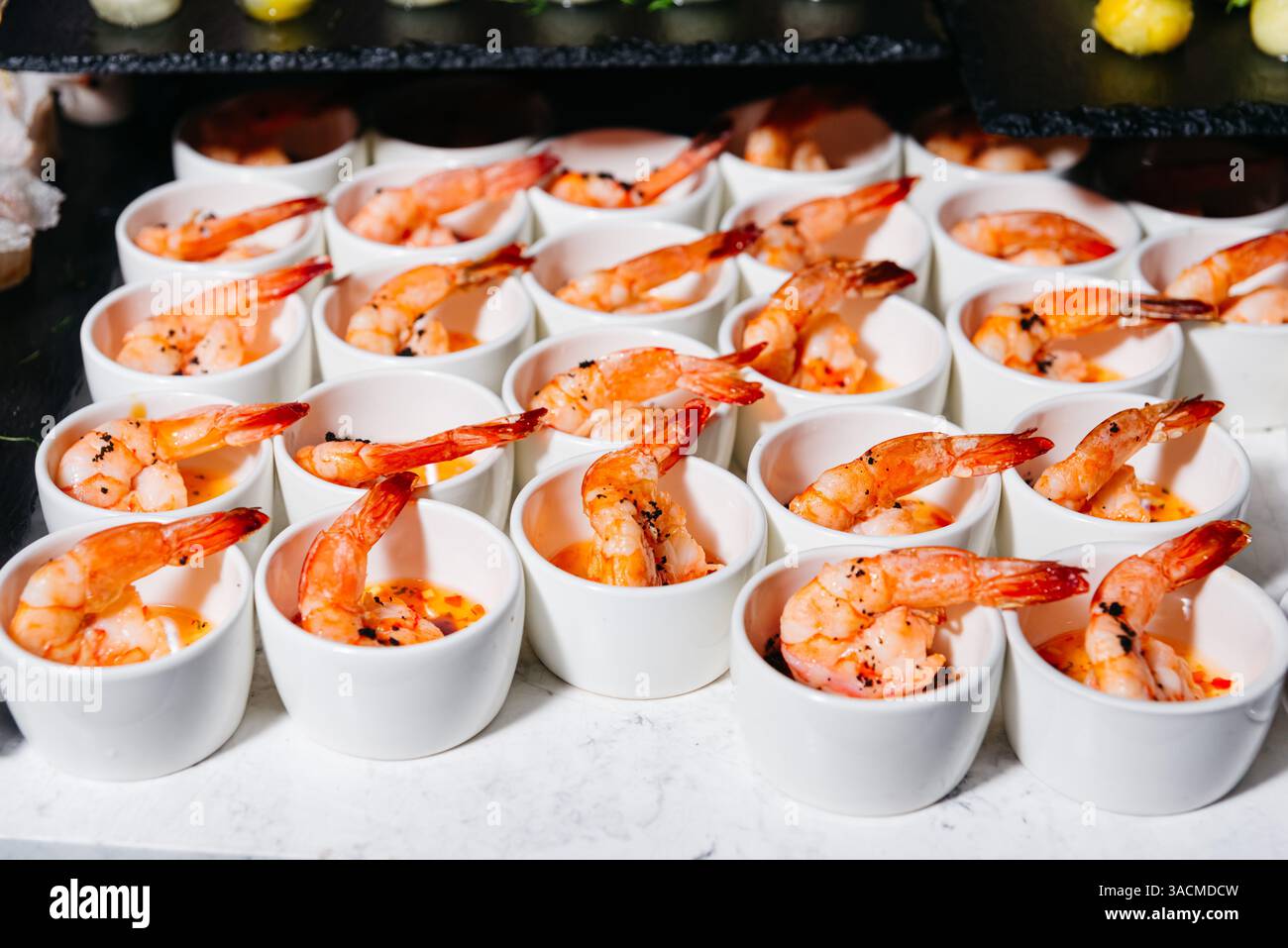 Gros plan de crevettes grillées épicées servies individuellement dans des tasses en céramique blanche, parfaites pour la restauration, les buffets ou les entrées de fête. Banque D'Images