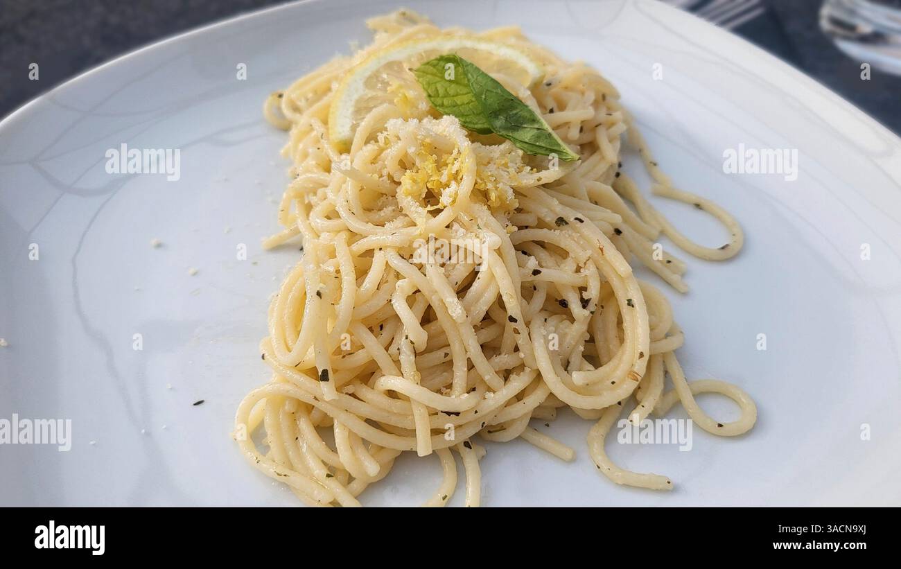 Assiette de spaghettis, simple et pourtant si attrayante. Les nouilles au parmesan, à la tranche de citron et à la feuille de menthe fraîche reposent lâchement sur une assiette blanche qui repose sur une base jaune. Banque D'Images