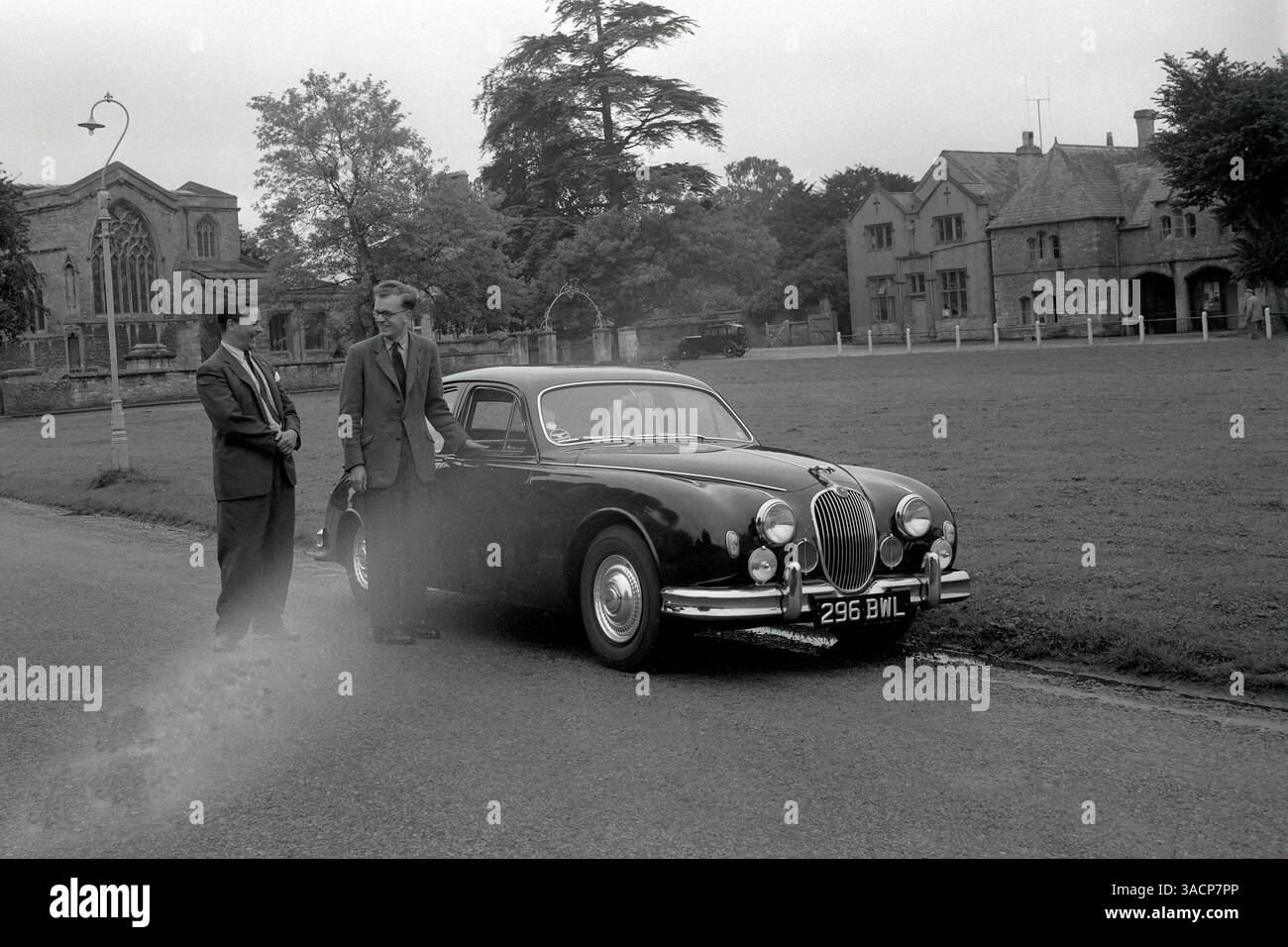Années 1950, historique, trois hommes devant une église à Oxford, Angleterre discutant de la voiture à côté d'eux, une berline Jaguar élégante, une voiture de luxe fabriquée en Grande-Bretagne par Jaguar Cars de Coventry. Fondée en 1922 sous le nom de Swallow Sideway Company, qui fabriquait des side-cars de moto, elle est devenue SS Cars en 1935. La première voiture Jaguar a été fabriquée en 1935, mais la société, alors détenue par Sir William Lyons, est officiellement devenue Jaguar Cars Ltd en 1945. Le nom Jaguar, précédemment utilisé sur les avions fabriqués par Armstrong Siddeley Co, est devenu synonyme de berlines sportives. Banque D'Images