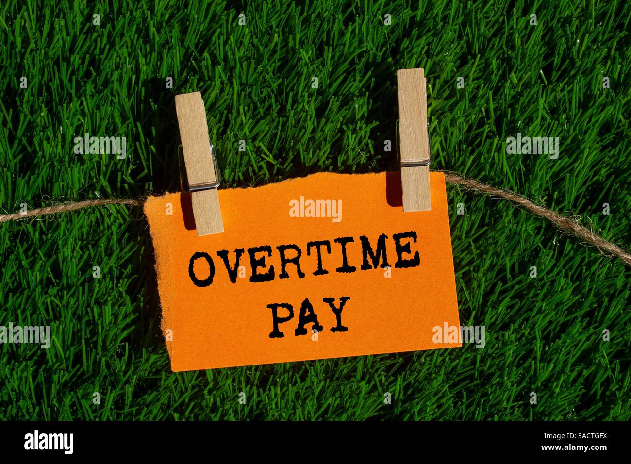 Message de paie d'heures supplémentaires écrit sur un morceau de papier orange déchiré déchiré sur fond d'herbe verte. Symbole conceptuel de rémunération des heures supplémentaires. Copier l'espace. Banque D'Images