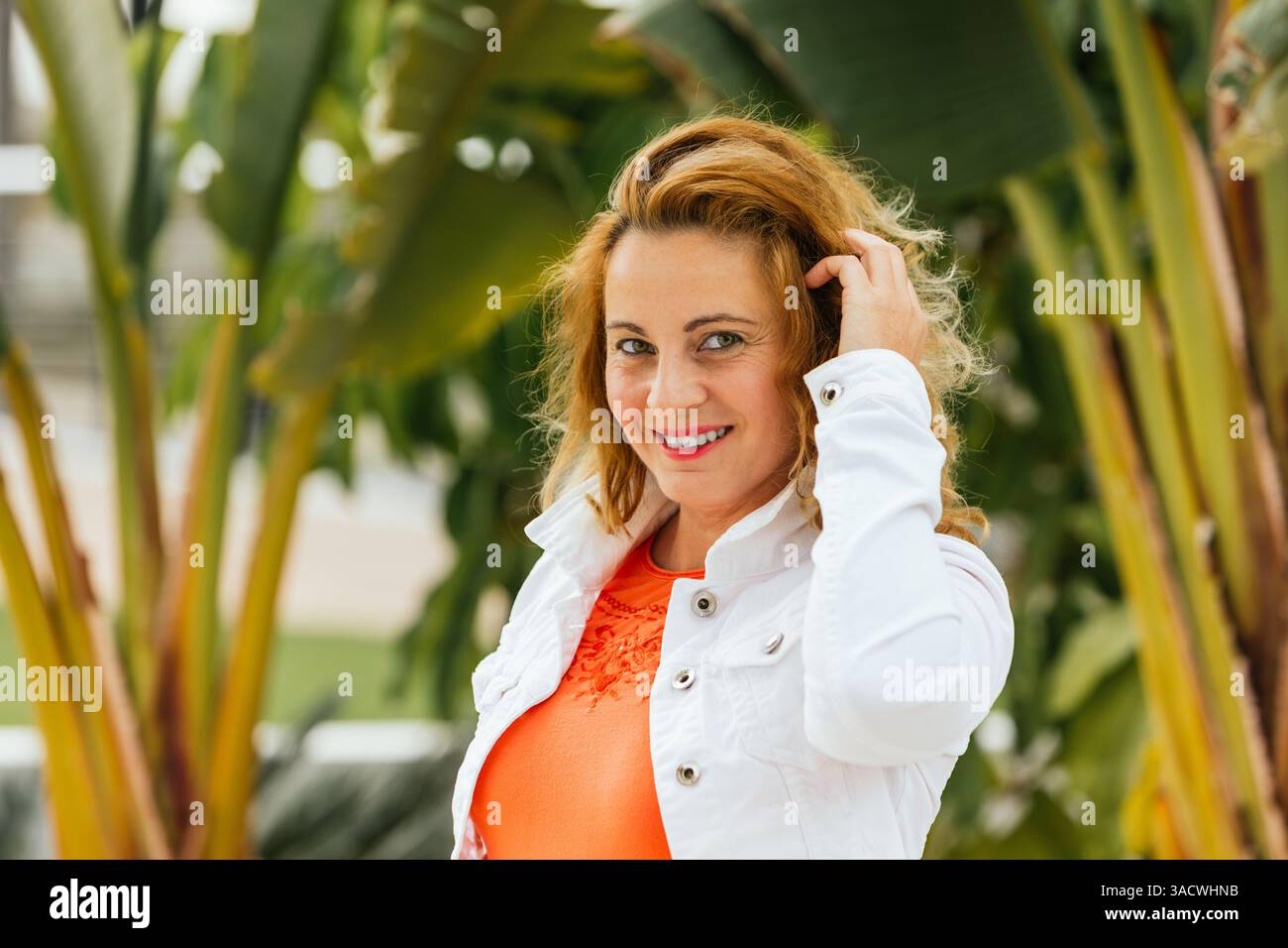 Femme souriante touchant les cheveux dans un jardin tropical. Jours fériés. Style de vie. Banque D'Images