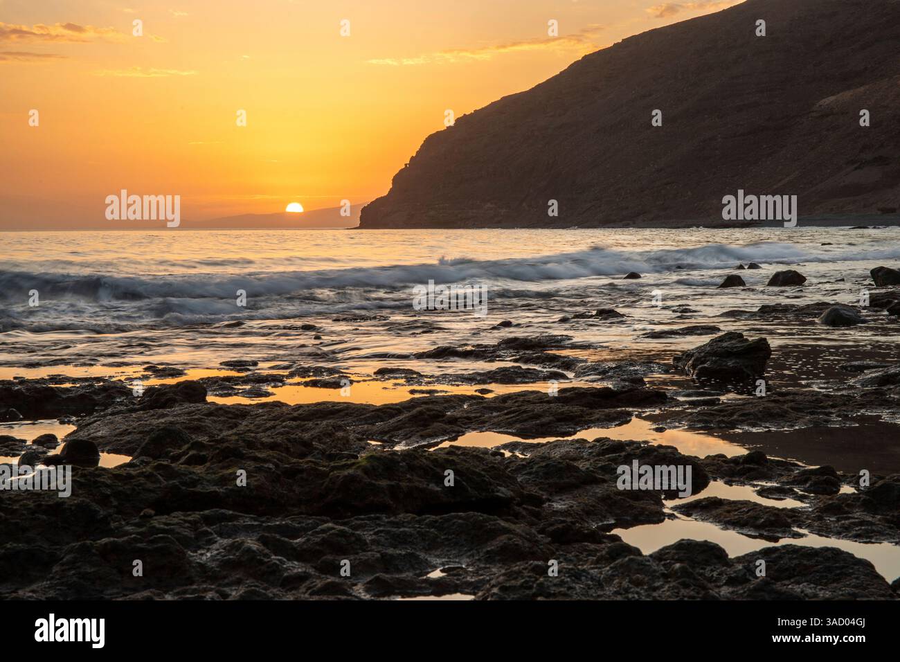 Coucher de soleil dans une baie. Beau paysage photographié avec une vue sur une côte aride à marée basse. À une lumière calima, sable du désert au crépuscule avec une grande couleur de ciel à Gran Tarajal, îles Canaries, Fuerteventura, Espagne Banque D'Images