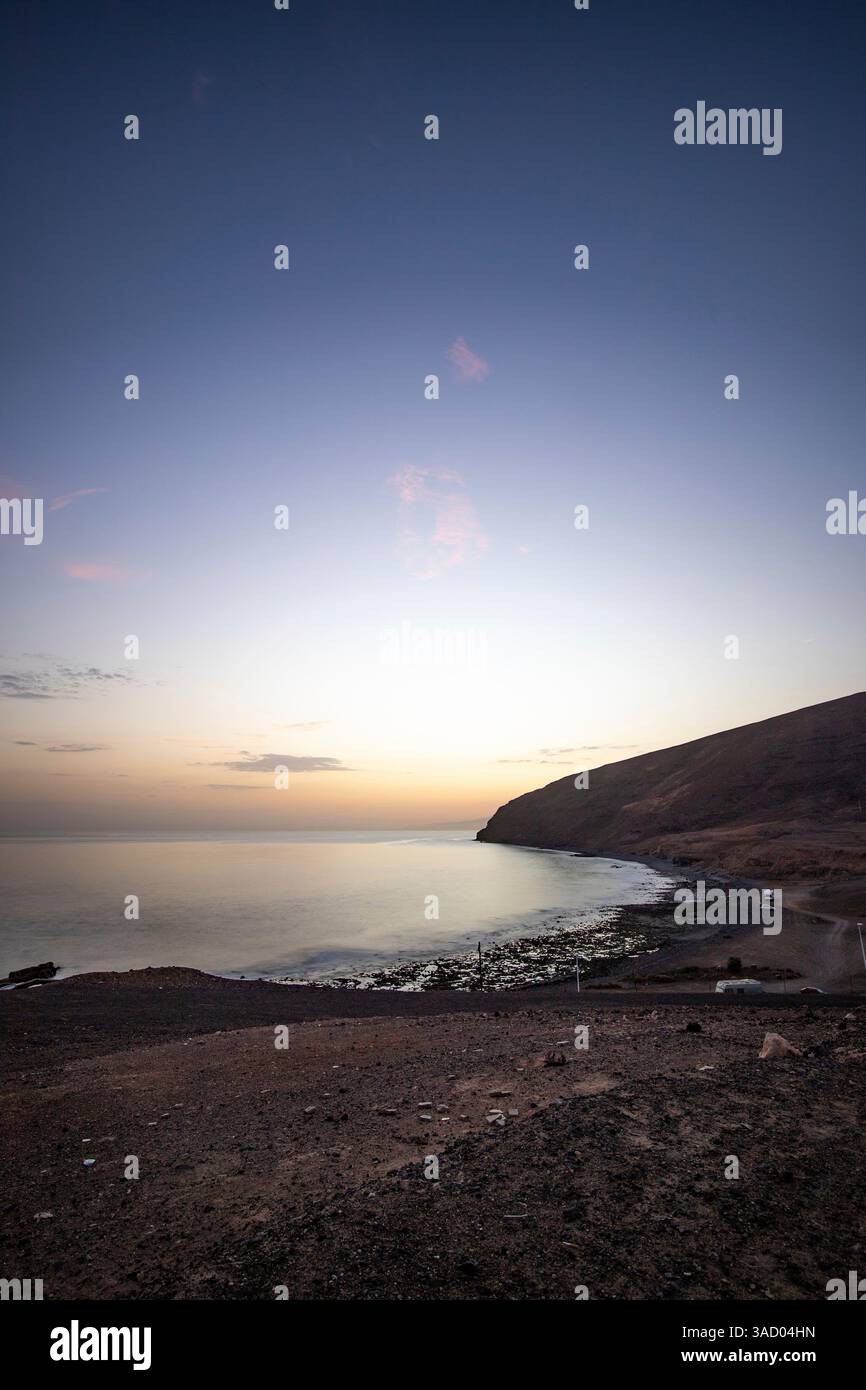 Coucher de soleil dans une baie. Beau paysage photographié avec une vue sur une côte aride à marée basse. À un léger calima, sable du désert au crépuscule avec une grande couleur de ciel à Gran Tarajal, îles Canaries, Fuerteventura, Espagne Banque D'Images