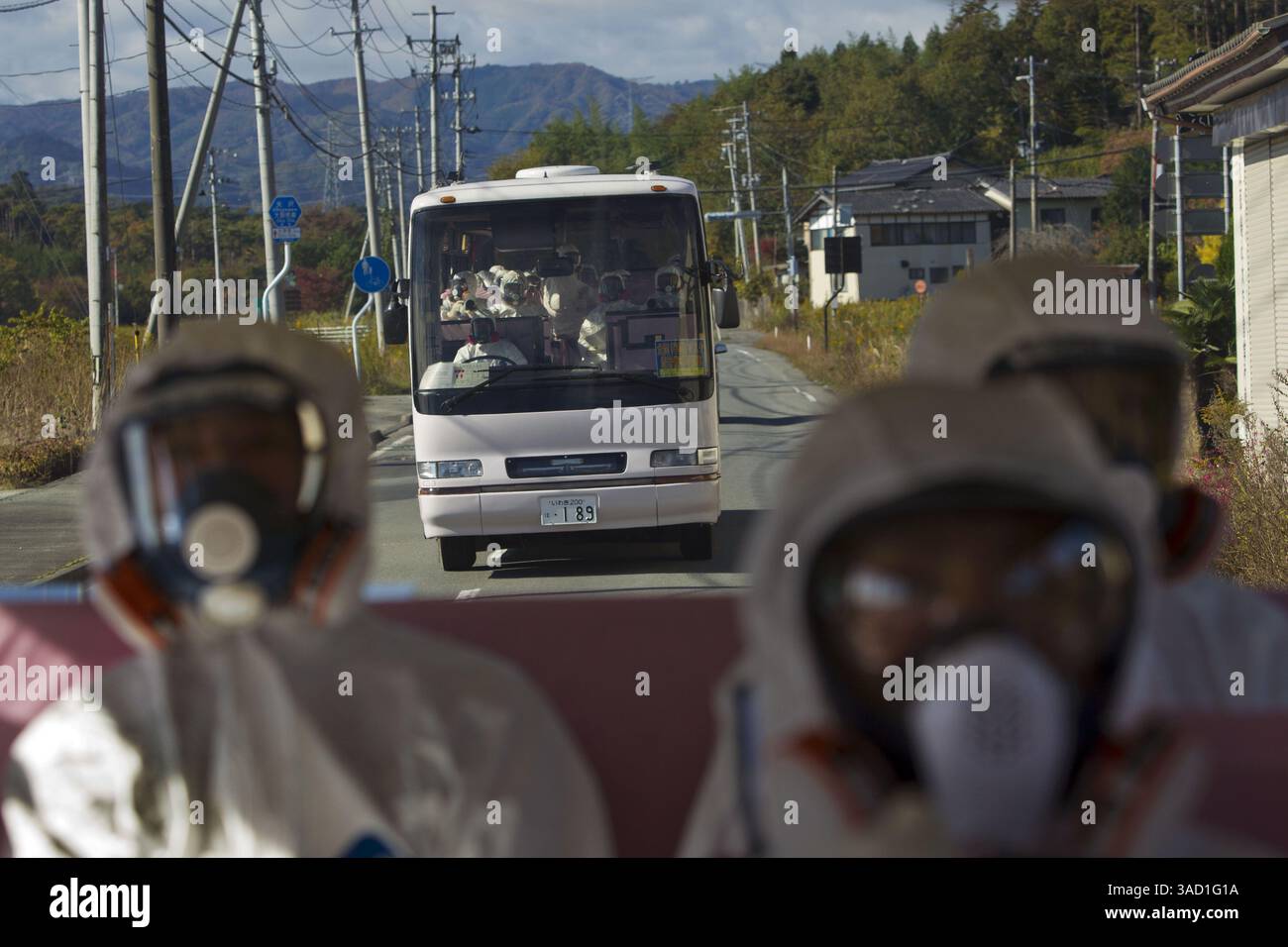 12 novembre 2011 - Tokyo, Japon - des officiels japonais portant des combinaisons de protection et des masques montent à l'arrière d'un bus tandis qu'un deuxième bus transportant des officiels et des journalistes japonais les suit alors qu'ils traversent la zone d'exclusion contaminée en route vers la centrale nucléaire paralysée de Fukushima Dai-ichi à Okuma, au Japon, samedi 12 novembre 2011. (Crédit image : © David Guttenfelder-Pool/Jana Press/ZUMAPRESS.com) Banque D'Images