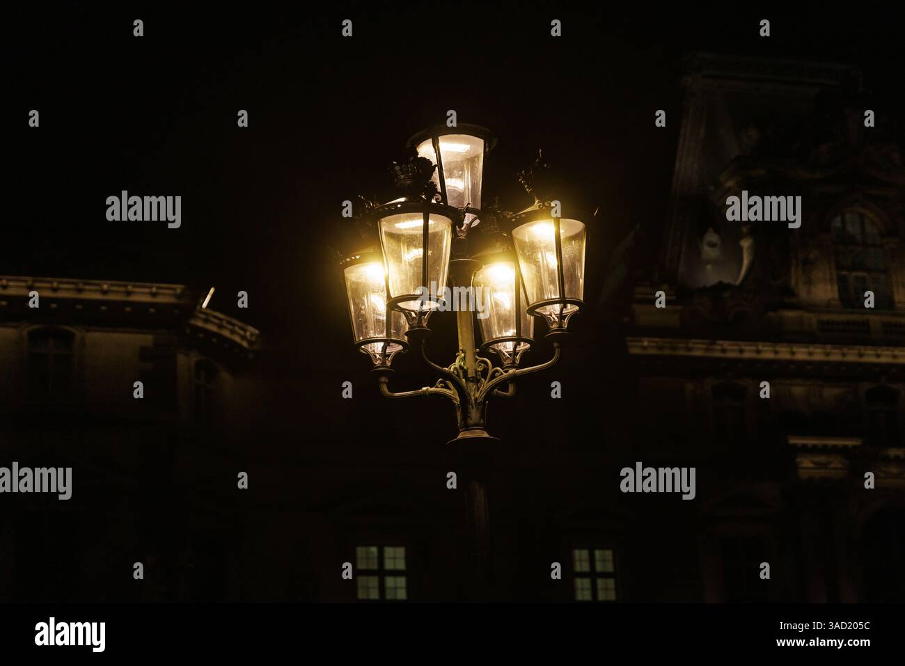 Un lampadaire avec cinq lumières est allumé la nuit. La lumière brille sur un bâtiment Banque D'Images