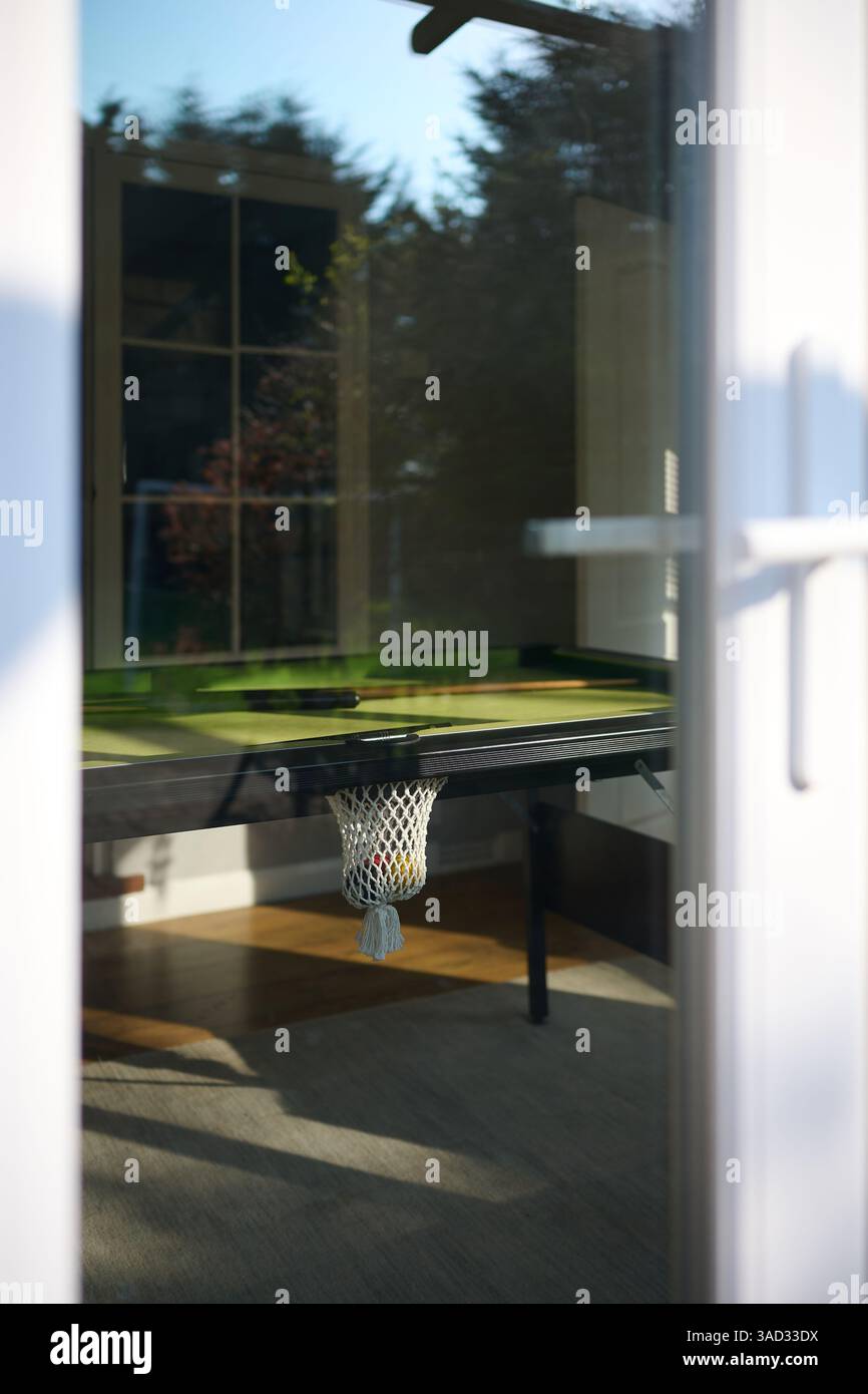 Vue ensoleillée sur une table de billard et poche de table de billard à travers une fenêtre de porte-patio Banque D'Images